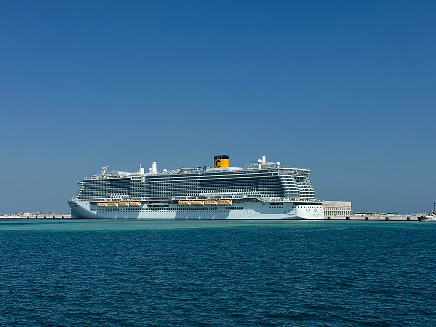 A cruise ship sitting in a harbour with blue sky and blue waters surrounding it on a sunny day.