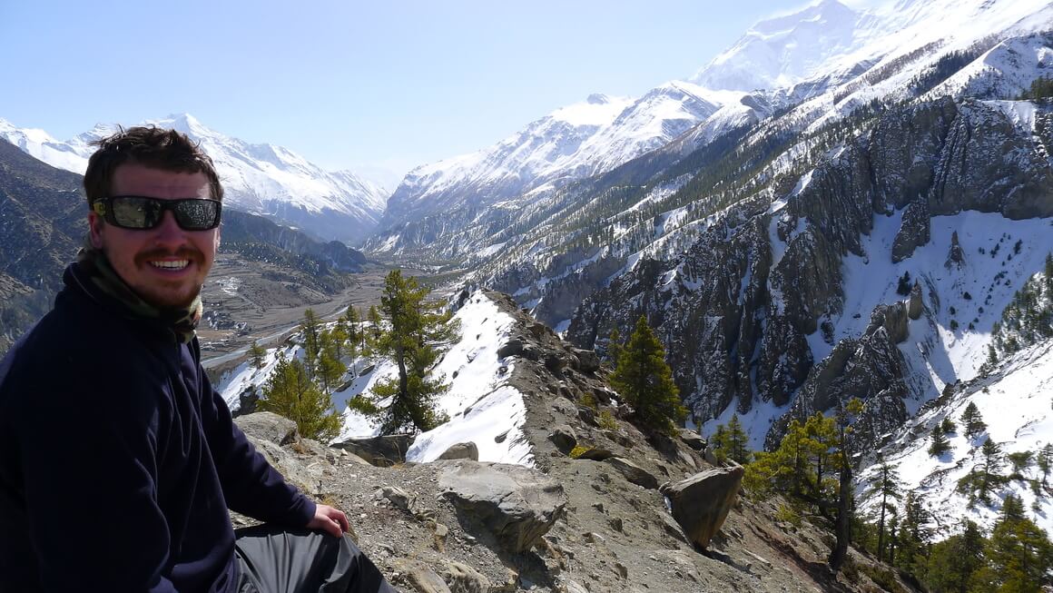 Will smiling in front of snowy mountains wearing his sunglasses