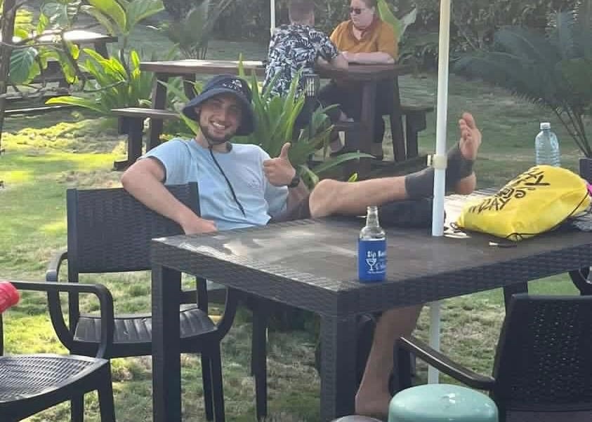 Joe smiling sitting with his foot in an ankle boot resting on a table