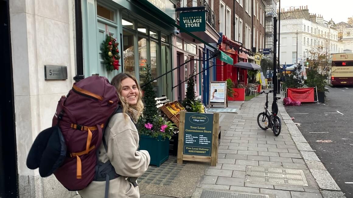 Dani smiling wearing a big backpacking walking in front of colourful shops