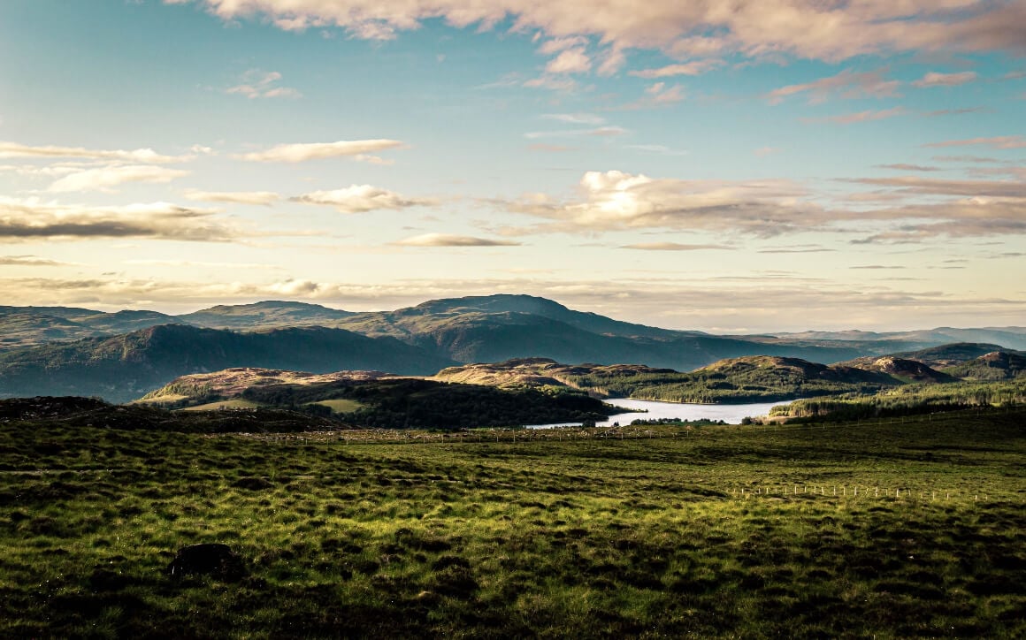 Grassy fields stretch toward a lake, framed by mountains in the backdrop in Inverness, Scotland