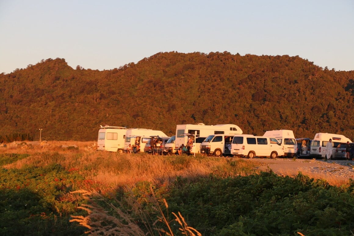 campervan parking in new zealand at sunset surrounding by green hills and grass