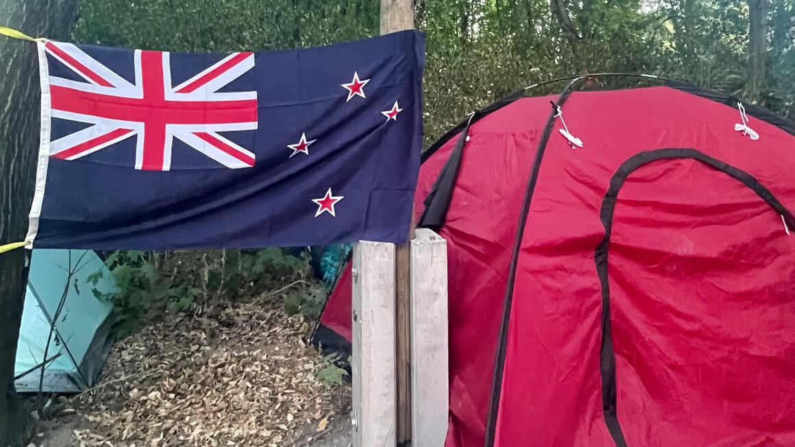 new zealand flag next to a red tent set up in the forest