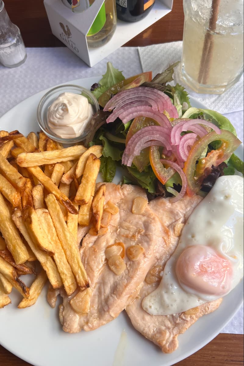a typical Portuguese meal, grilled chicken, a fried egg, french fries, and a salad  