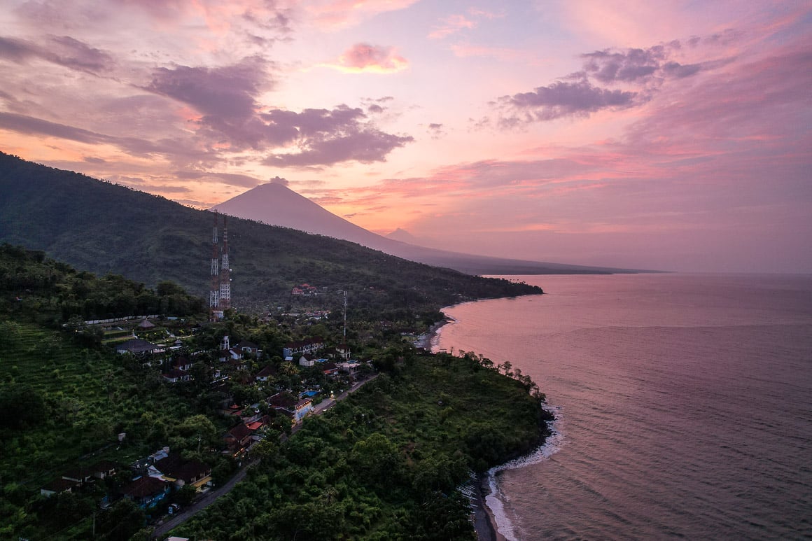 pink and purple sunset over mt agung in bali with the lush green hills of amed town coming in the forefront