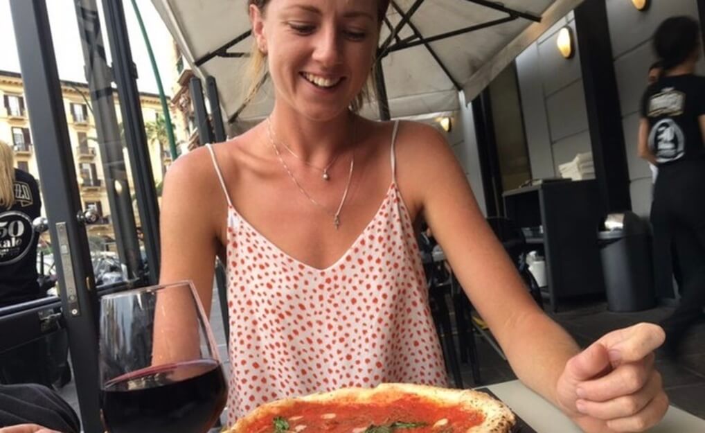 A woman smiling lovingly at a pizza with a glass of red wine
