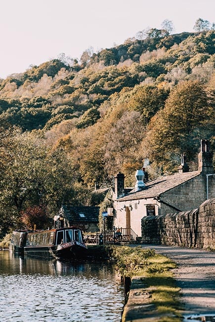 Looking down the Rochdale Canal to see a stone built pub and a barge parked up outside it near Hebden Bridge, Yorkshire