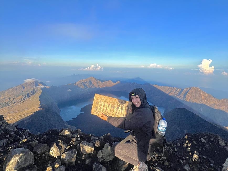 Taya at the summit of Mt Rinjani on Lombok holding a sign with the name of the mountain