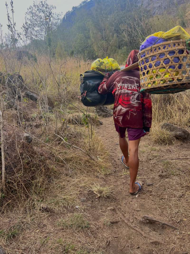 a porter hiking up mount rinjani with a huge load of gear carried in baskets