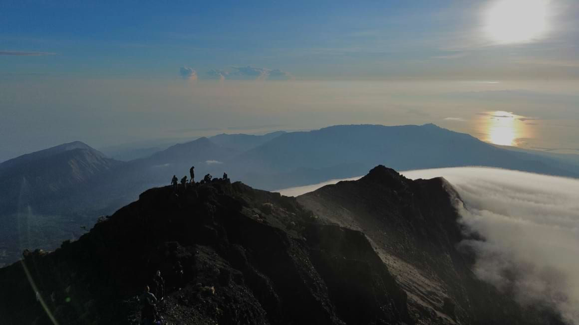 a drone shot of people standing on the mount rinjani summit during sunrise with clouds inverted