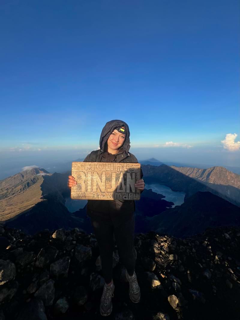 taya at the mount rinjani summit taking a picture with a sign