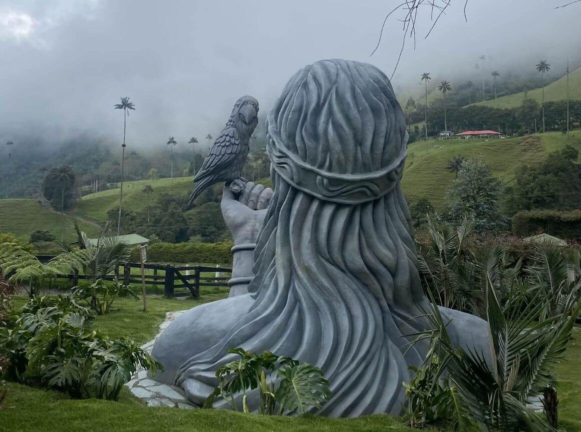 big silver statue of a man holding a bird at at cocora valley in colombia