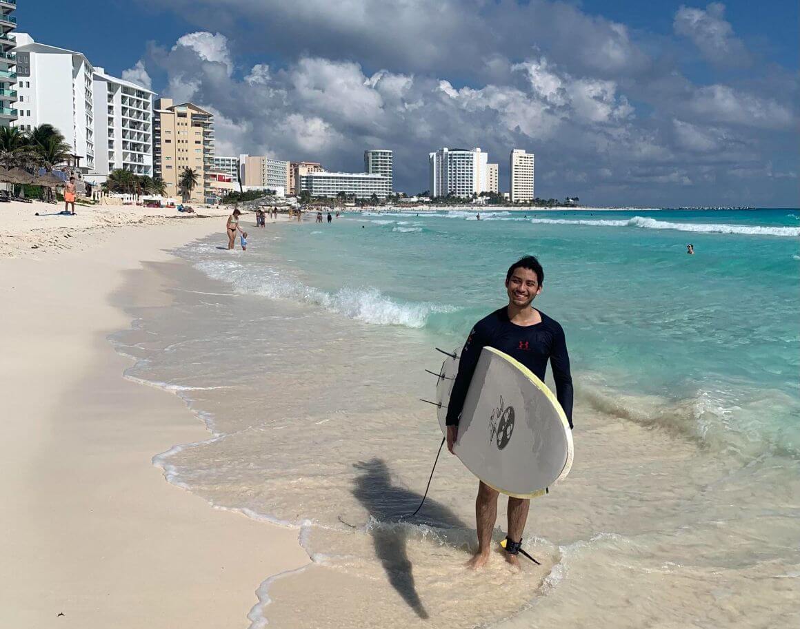 person standing on the beach hwith a surfboard in cancun