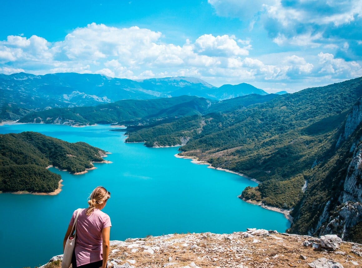 girl walking on a cliff above the turquoise blue bovilla lake in albania