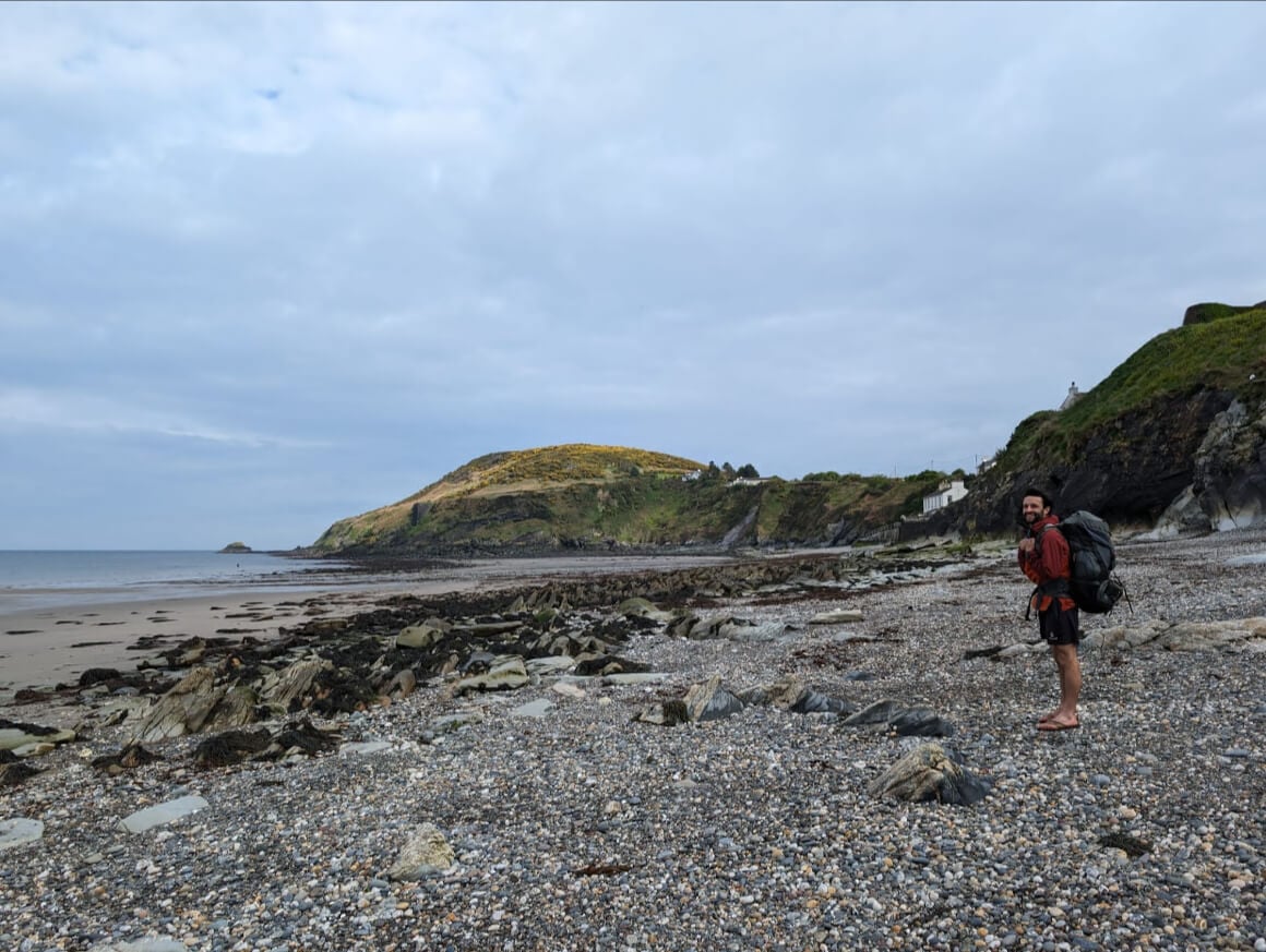 guy with a Backpack standing on a rocky coastal beach on the isle of man