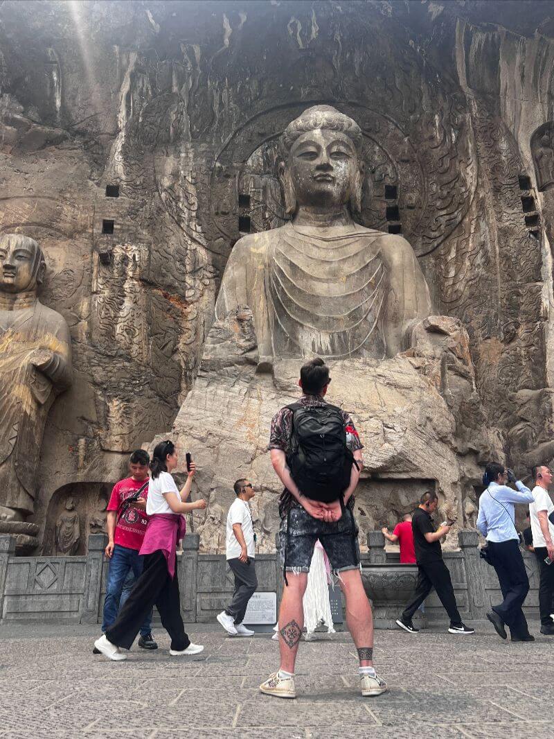 man looking at big sculptured buddha statue with walking crowds