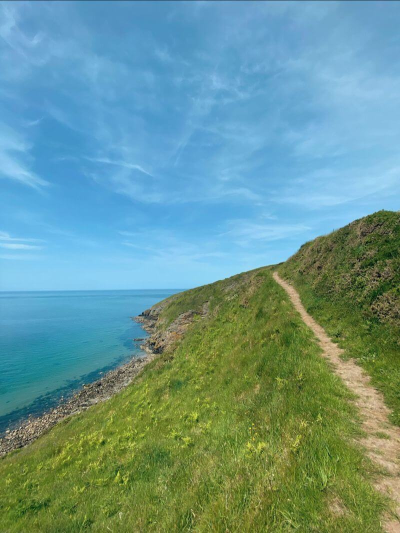 view of clear blue skies, sea and grassy mountain with pathway