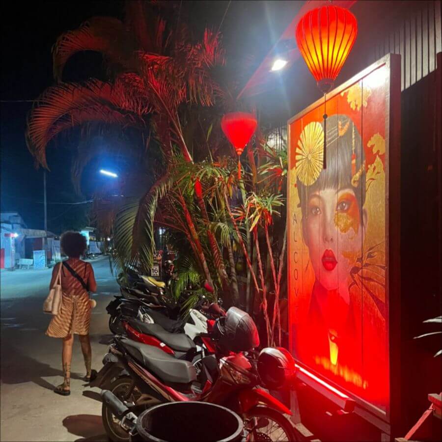 female traveller beside a lanterned shop and parked motorbikes