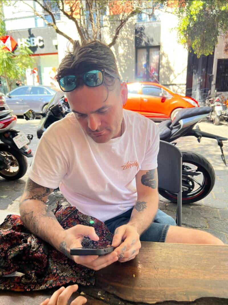 man using phone, sitting on an outdoor cafe with parked vehicles around