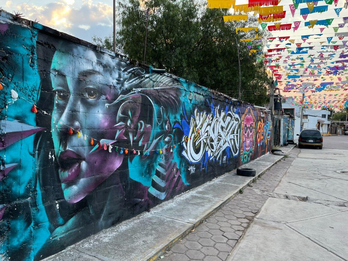 empty street with a wide wall of art murals and hanging festive banners.