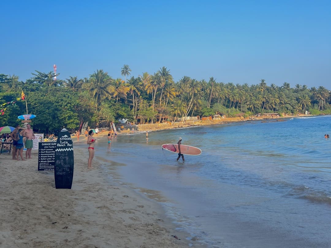 man heading out to surf on hiriketiya beach, sri lanka