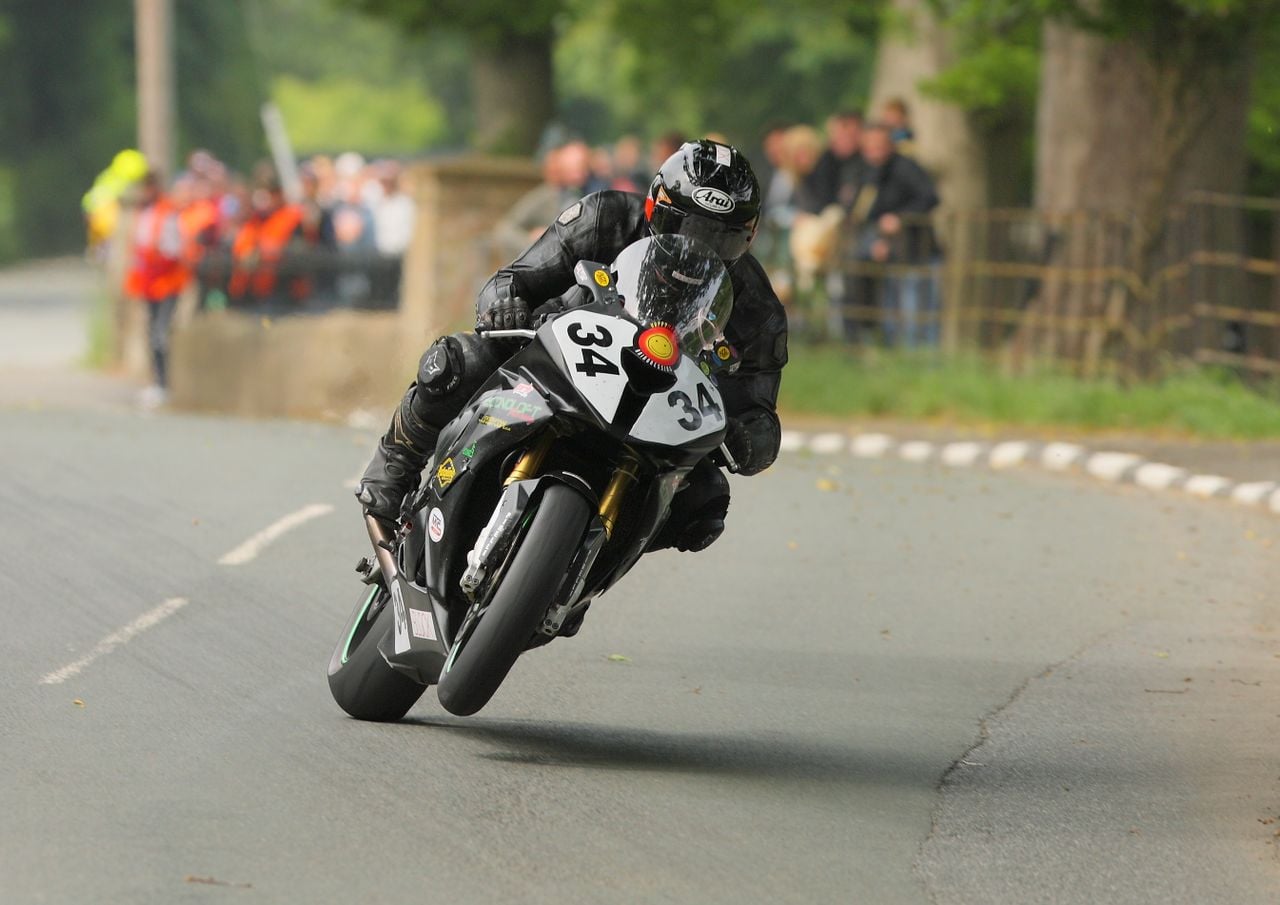 man wearing black on a black motorbike racing in the isle of man tt