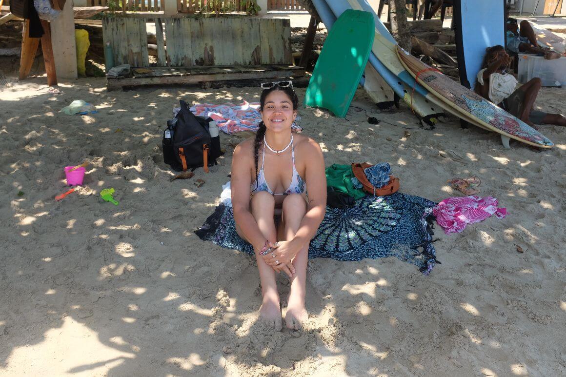 female traveller sitting on the sandy beach, shaded by a tree