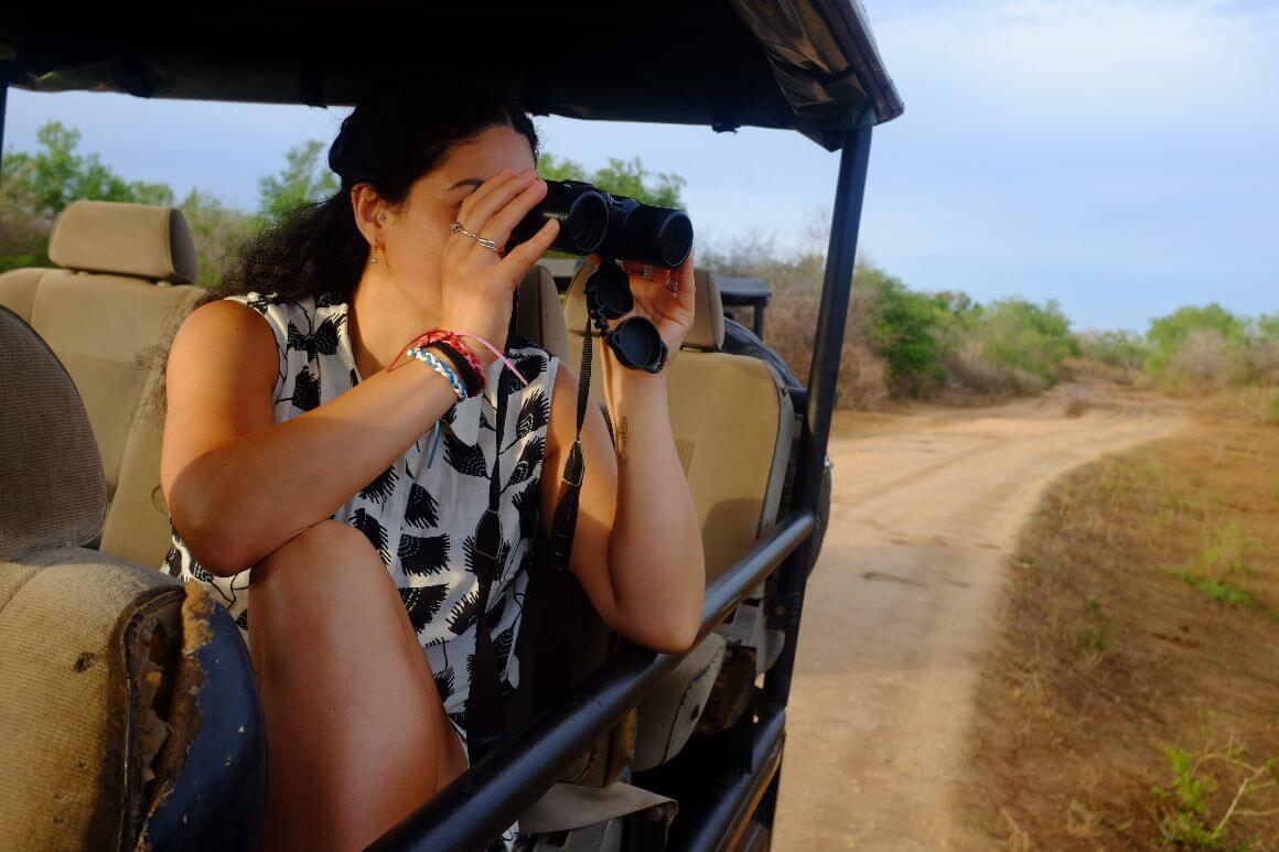 female traveler looking at binoculars while riding a safari jeep