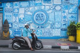 local man in canggu bali sitting on scooter in front of a bright blue wall decorated in street art