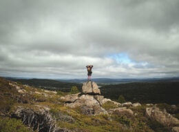 Person stood on top of rock with both hands behind their head overlooking green rolling hills