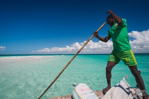 A man wearing a bright green outfit pushing a bamboo stick into crystal clear waters of Mozambique Africa
