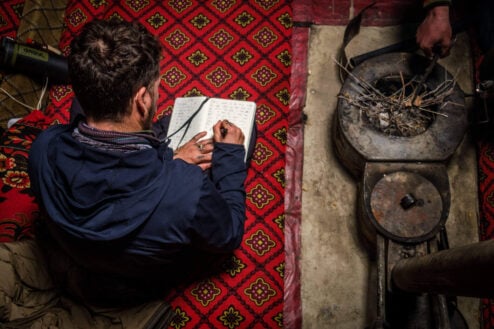 Will writing in his journal in Pakistan whilst sitting on a patterned rug next to a fire that is about to be lit