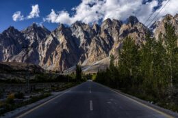 a massive wall of mountains towering over a paved black highway in hunza valley northern pakistan
