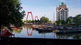 Image over canal of the Rotterdam city skyline with red arch bridges.