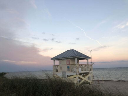 a lifeguard hut on the sand behind beach sea grass during a light pink pastel sunset at key biscayne beach in miami florida