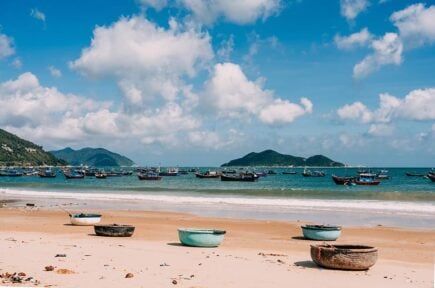 Round conical boats on the beach with mountains in the background in Vietnam