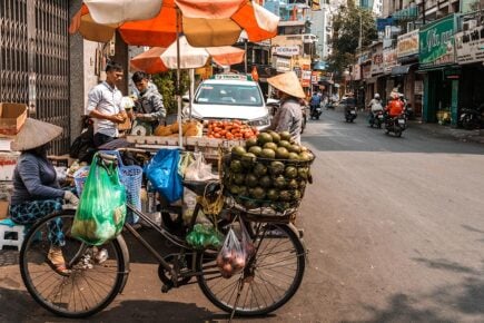 A street food stall on a street in Vietnam with a fruit seller on a bike.