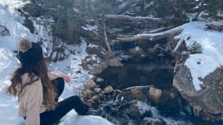A girl sitting next to the river as it snows in the mountains of Utah, usa United States of America.